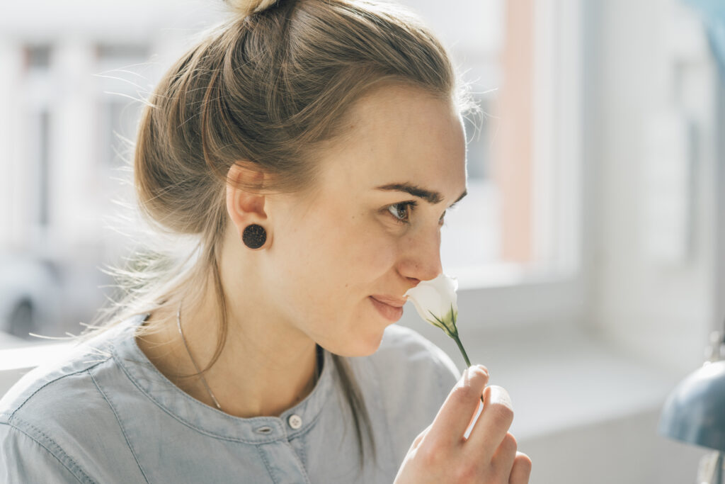 A young woman smelling a white, blossoming flower.