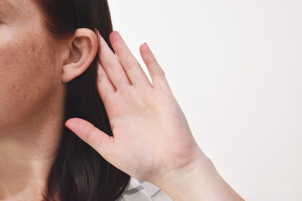 Close up of a woman putting her hand towards her ear so she can hear better.