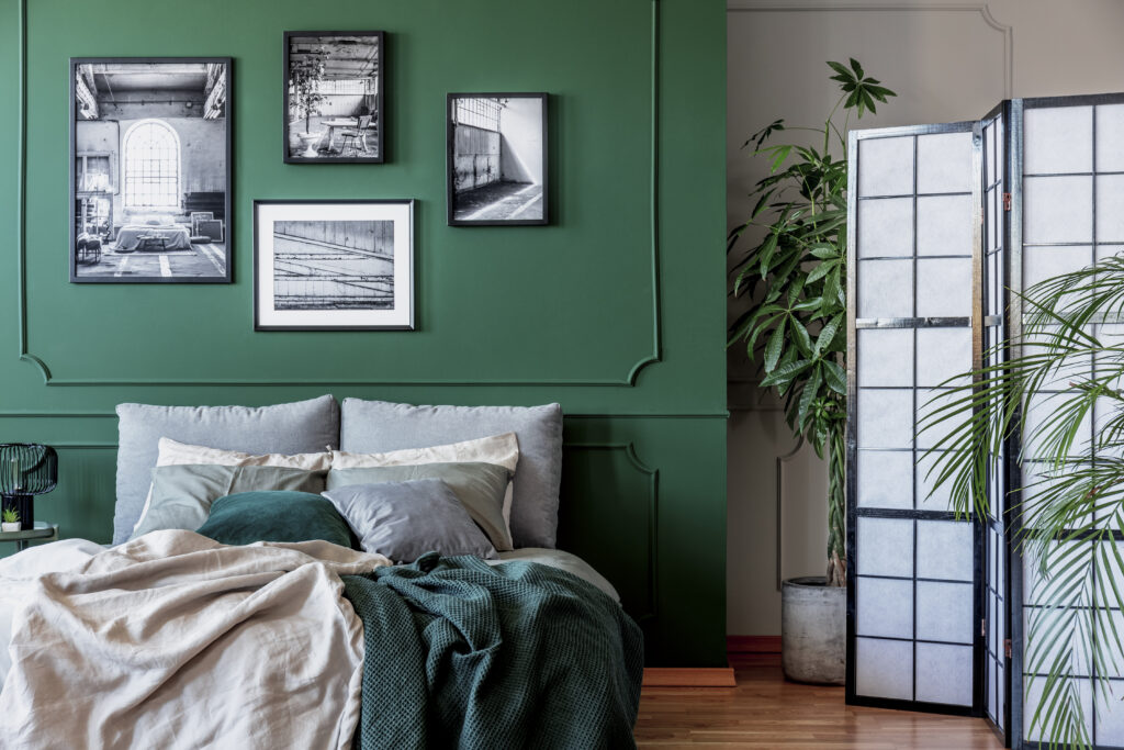 Gallery of black and white posters and photos on emerald green wall in trendy bedroom.