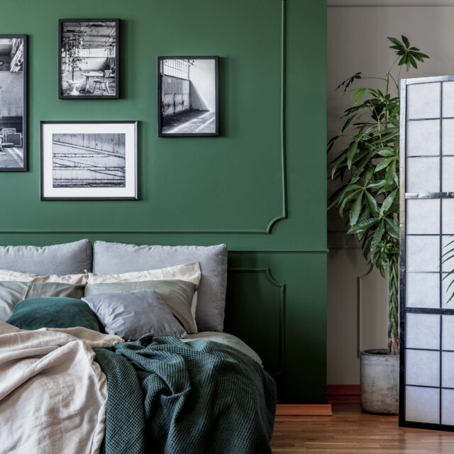 Gallery of black and white posters and photos on emerald green wall in trendy bedroom.