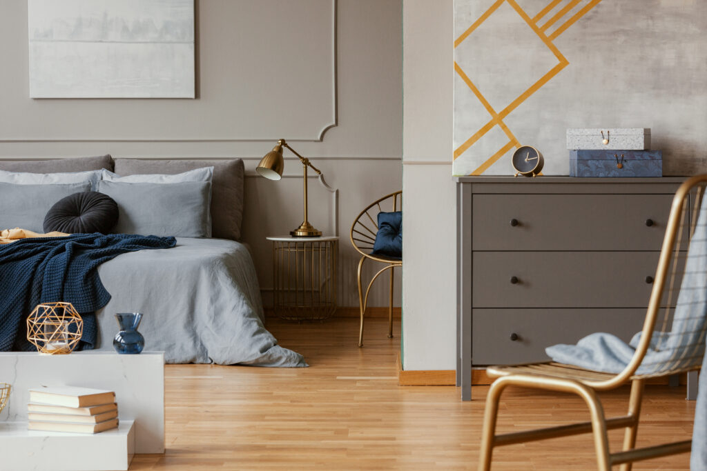 Trendy bedroom interior with grey commode and golden chair.