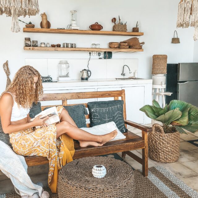 Blonde woman dressed in summer clothing reading a book in a stylishly-designed living room.