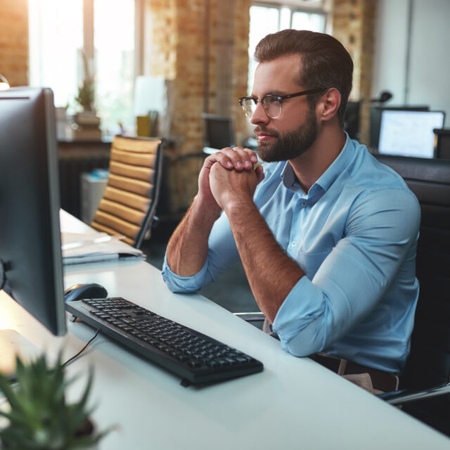 A Side View of a Pensive Bearded Man with Eyeglasses Looking at a Computer Screen