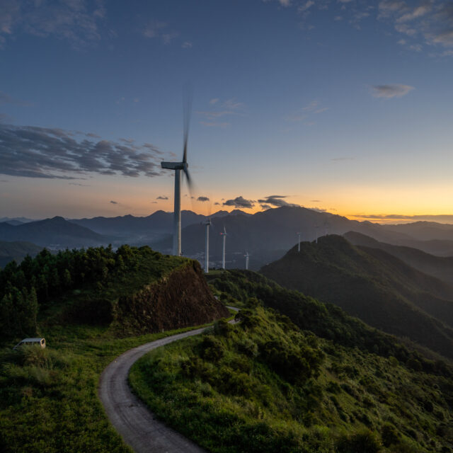 Picture of a wind turbine in the mountains overlooking a sunset.